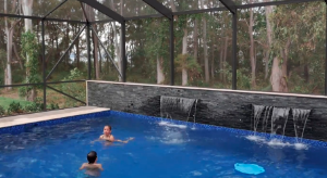 Two children swimming in a pool cage with a stone wall and waterfalls.